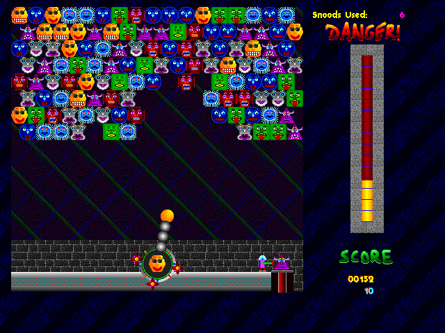 Snood gameplay screen with launcher at bottom and grid of face-blocks at top